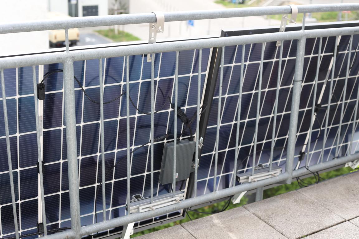 Der Wechselrichter ist im Test am Solarmodul angebracht und hängt verbunden mit 2 Solarmodulen an einem Balkongeländer.